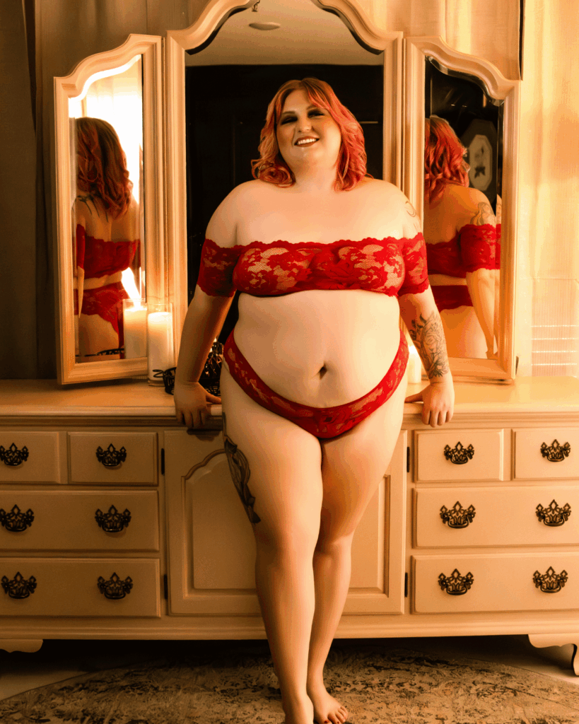 Woman in red lingerie smiling in front of a mirror during a boudoir photography session in Evansville, Indiana.