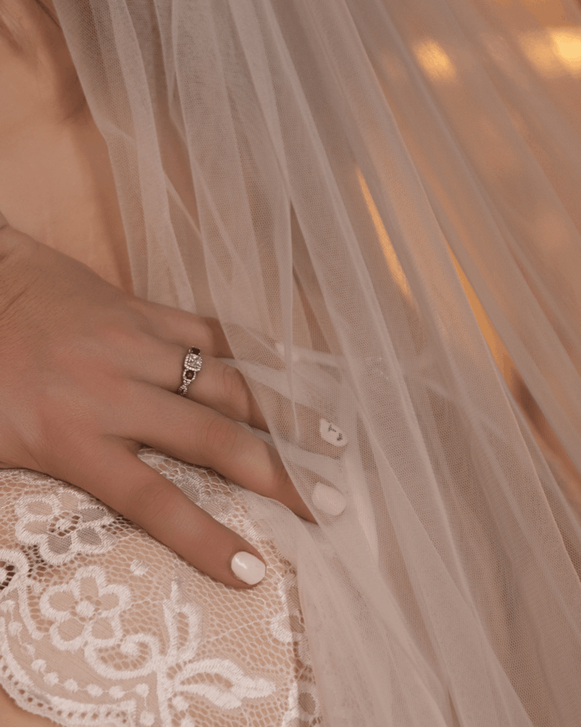Close-up of a bride's wedding ring resting on lace and bridal veil during a bridal boudoir session.